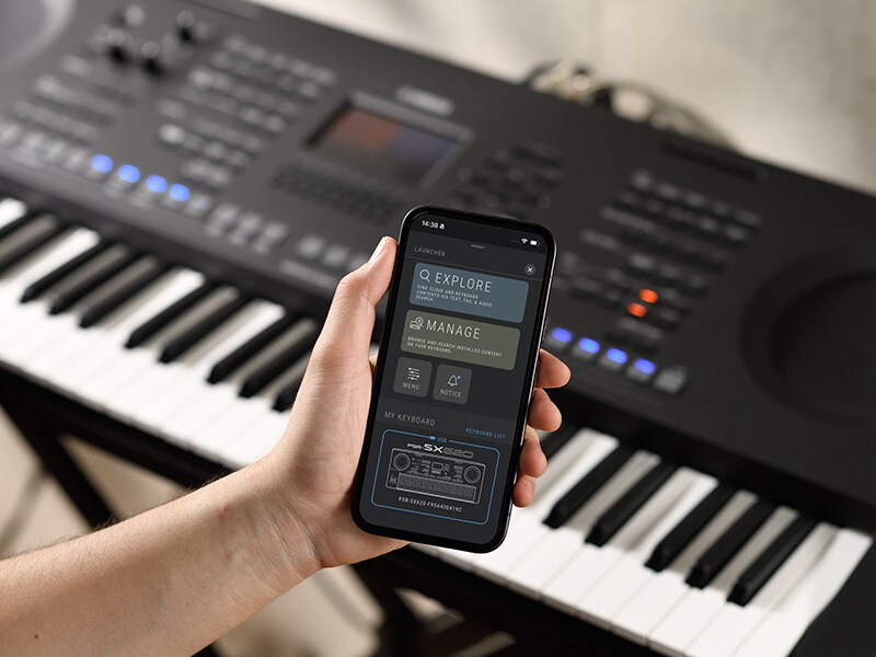 PSR-SX920 y una mano sosteniendo un smartphone con la pantalla de un reproductor de música.