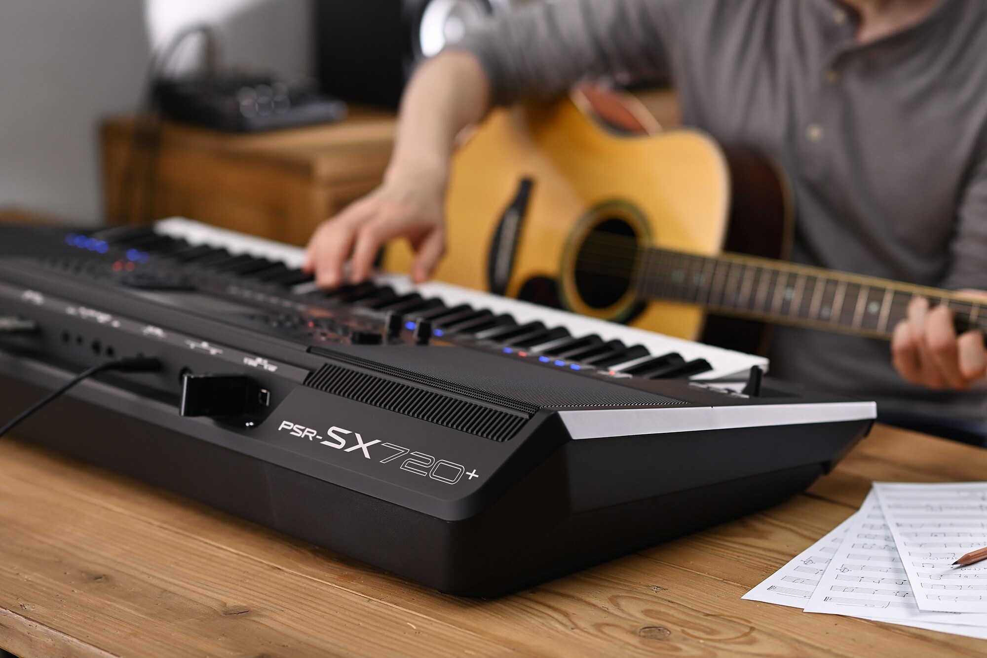 Foto de una persona tocando la estación de trabajo de arreglos Yamaha PSR-SX720+ mientras sostiene una guitarra