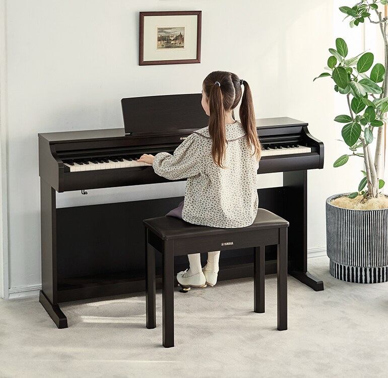 Una niña practicando en un piano ARIUS en una sala de estar