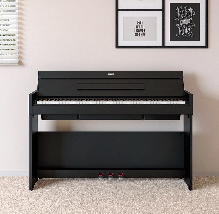 Una sala de estar que cuenta con un piano ARIUS color negro colocado junto a estantes de pared en los que se encuentran lámparas y un difusor, armoniosamente integrado con la decoración.
