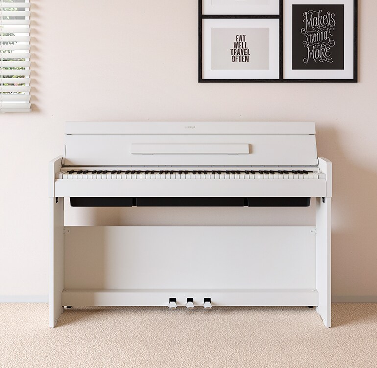Una sala de estar que cuenta con un piano ARIUS color blanco colocado junto a estantes de pared en los que se encuentran lámparas y un difusor, armoniosamente integrado con la decoración.