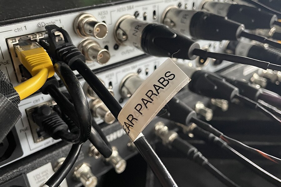 Acercamiento de las conexiones del equipo de audio que muestra los cables de red Dante y las salidas de los micrófonos parabólicos